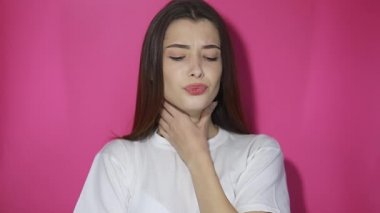Boğazı ağrıyan, nefes nefese kalan boyun, gırtlak iltihabı olan solunum enfeksiyonu, grip belirtileri, bademcik iltihabı ya da tiroid bozuklukları olan bir kız. Stüdyo çekimi pembe arkaplanda izole edildi