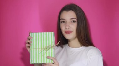 Çekici bir kadın hediyesini yakalıyor ve kutusunu kameraya veriyor, Noel hediyesini paylaşıyor arkadaşça gülümsüyor, tatilleri kutluyor, doğum gününü kutluyor. Stüdyo çekimi pembe arkaplanda izole edildi