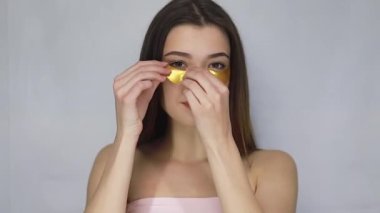 Güzellik, insanlar ve sağlık konsepti. Harika esmer bir kadının çıplak portresi. Daha iyi ve taze görünmek için gözlerinin altına altın bantlar takıyor. Güzel model kız kameraya gülümsüyor..