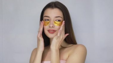 Güzellik, insanlar ve sağlık konsepti. Harika esmer bir kadının çıplak portresi. Daha iyi ve taze görünmek için gözlerinin altına altın bantlar takıyor. Güzel model kız kameraya gülümsüyor..