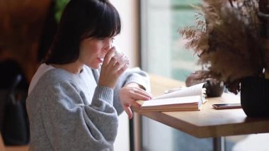 Güzel genç bayan kafede kitap okuyor. Modern edebiyat ve yalnızlığın tadını çıkarıyor. Masada tek başına oturuyor. Mutlu binyıllar, hobi ve gençlik yaşam tarzı konsepti.