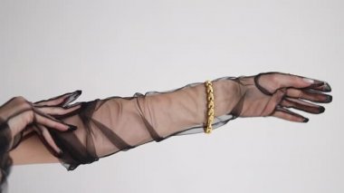 Elmas yüzüklü, büyük, kalın altın bir zincir ve bir bilezik tutan bir kızın yakın çekimi. Lüks bir hayat. Mücevher reklamı. Gri arka plandaki stüdyoda. Kolundaki bilezik.