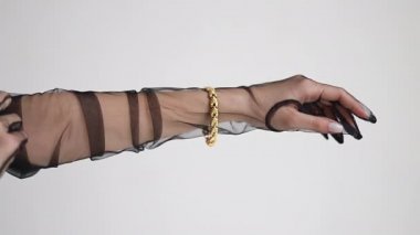 Elmas yüzüklü, büyük, kalın altın bir zincir ve bir bilezik tutan bir kızın yakın çekimi. Lüks bir hayat. Mücevher reklamı. Gri arka plandaki stüdyoda. Kolundaki bilezik.