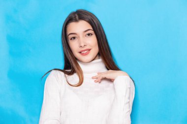 Gülümseyen, beyaz elbiseli, soluk mavi arka plan stüdyo resminde soyutlanmış bir şekilde poz veren esmer kadın. İnsanlar yaşam tarzı kavramını hisseder. Kopyalama alanı oluşturun. Kameraya bak