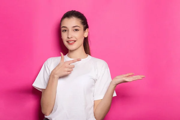 분홍색 배경에 체크무늬 셔츠를 제품의 공간을 손가락질하는 여학생의 — 스톡 사진