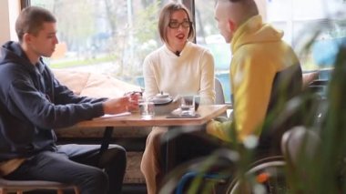 Kafedeki tekerlekli sandalyedeki mutlu genç adam arkadaşlarıyla iletişim kuruyor. Çeşitli takımlar kafede birlikte çalışıyor, bir online teknoloji firması pazarlama stratejisi için beyin fırtınası yapıyorlar..