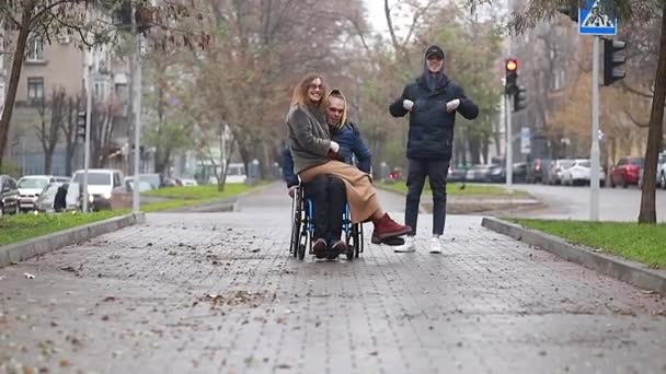在秋天或春天 坐在轮椅上的可爱的残疾人抱着一个女孩在城市里走来走去 — 图库视频影像