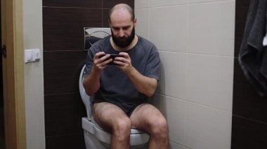 Tuvalette oturan adam akıllı telefon kullanıyor. Genç Latin adam tuvalette oyun oynuyor.