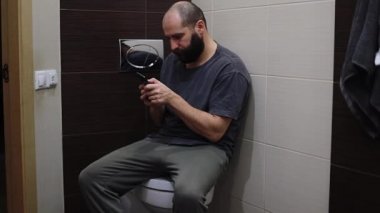 Genç çocuğun ellerinin modern cep telefonunu tutarken çevrimiçi video oyunları oynamak için oyun uygulaması kullanırken kapak kapağıyla tuvalette oturan ebeveynlerden saklandığı yakın plan..