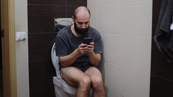Young Man Sits Toilet Restroom Looks Smartphone Surprised Something — Stock Video