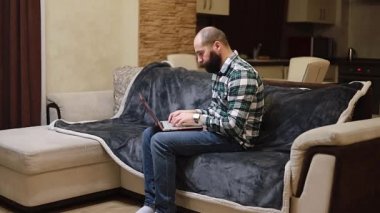 Adam dizüstü bilgisayarını kullanarak kanepeye oturuyor. Ekran daktilo iş mesajlarına bakıyor. Spbd 'de hipster sohbetleri yapıyor. İnternette sörf yapmak, sosyal medya okumak veya evde çalışmak