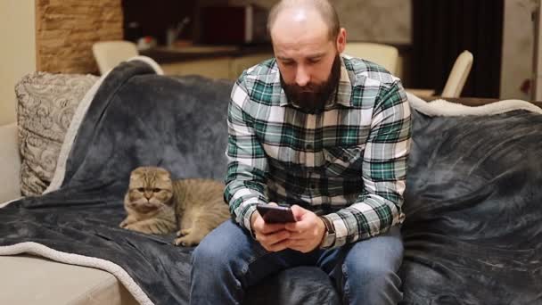 Młody Człowiek Używa Smartfona Leży Kanapie Kotem Domowym Przytulnym Domu — Wideo stockowe