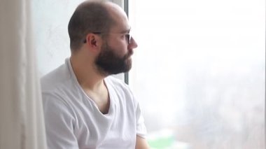 Yalnız adam ne yazık ki pencereden dışarı bakar, yakından. Genç adam bir fincan kahve ya da çayla pencereye doğru yürür ve yüzünde düşünceli bir ifadeyle bir yudum alır.