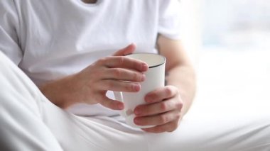 Şehir manzaralı bir pencere pervazında otururken dizüstü bilgisayarıyla çalışan genç bir adamın el kamerası görüntüsü. Evden çalışan serbest çalışan biri. Çay içen adam