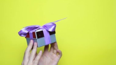 Kırmızı kurdeleli bir adamın eline yakın çekim. Noel, yeni yıl, doğum günü, Sevgililer Günü, uluslararası kadınlar günü sürprizi. Kişi sarı kutuda duruyor, 4k görüntü