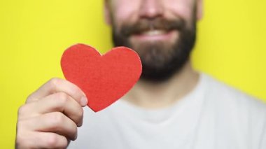 Ellerinde küçük kırmızı bir kalp var. Sevgililer Günü konsepti. Adam kırmızı kalp yeteneği gösteriyor. Aşk ve Mutluluk kavramı. Yakışıklı sakallı adam, sevgililer günü konseptine kağıt kalp veriyor.