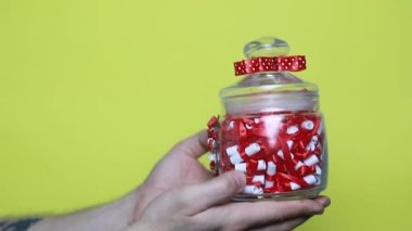 Kırmızı kurdeleli bir adamın eline yakın çekim. Noel, yeni yıl, doğum günü, Sevgililer Günü, uluslararası kadınlar günü sürprizi. Kişi sarı kutuda duruyor, 4k görüntü