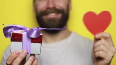 Çekici bir adamın portresi, el kâğıdı kalp şeklinde bir kart, sıradan bir gömlek giyer. Erson sarı kutuda duruyor, 4k görüntü.
