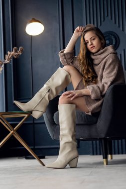 Annesinin süet çizmeleriyle poz veren saçları olan çekici bir kız. Çocukluk, genç aktris, cazibe. Tam boy çekim, izole edilmiş iç plan. 7-9 yaşlarında bir kız. Eller yüze..