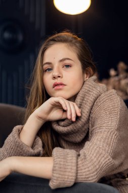 Kahverengi kazaklı küçük kız, sonbahar elbiseli şirin küçük kız. Uzun saçlı, gülümseyen güzel bir kızın portresi. 7-9 yaşlarında bir kız. Eller yüze..