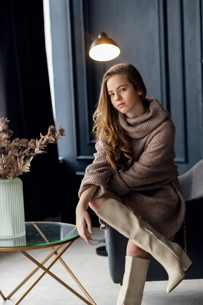 Annesinin süet çizmeleriyle poz veren saçları olan çekici bir kız. Çocukluk, genç aktris, cazibe. Tam boy çekim, izole edilmiş iç plan. 7-9 yaşlarında bir kız. Eller yüze..