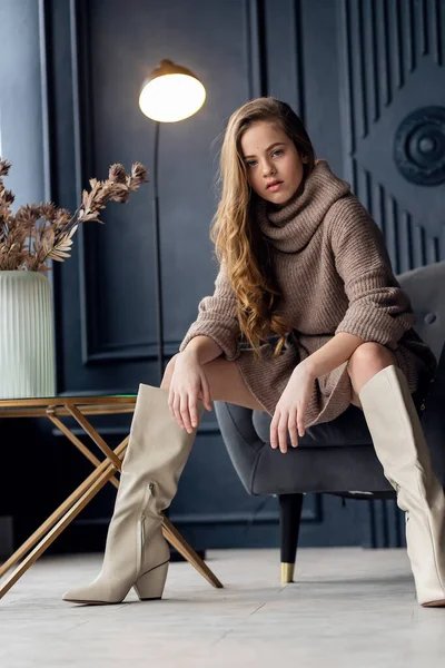 Annesinin süet çizmeleriyle poz veren saçları olan çekici bir kız. Çocukluk, genç aktris, cazibe. Tam boy çekim, izole edilmiş iç plan. 7-9 yaşlarında bir kız. Eller yüze..