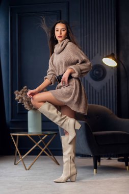 Güzel bir iç mekanda bej çizmeli güzel esmer kadın. Tam boy portre. Bej renkli şık giyinen zarif bir bayan. Uzun kahverengi dalgalı saçlı güzel kız. Modaya uygun bir bayan.
