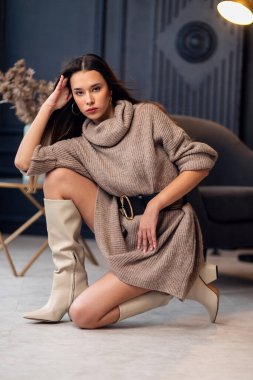 Güzel bir iç mekanda bej çizmeli güzel esmer kadın. Tam boy portre. Bej renkli şık giyinen zarif bir bayan. Uzun kahverengi dalgalı saçlı güzel kız. Modaya uygun bir bayan.