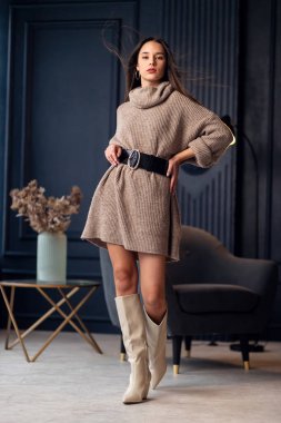Güzel bir iç mekanda bej çizmeli güzel esmer kadın. Tam boy portre. Bej renkli şık giyinen zarif bir bayan. Uzun kahverengi dalgalı saçlı güzel kız. Modaya uygun bir bayan.