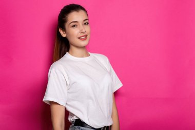 Beyaz tişörtlü çekici kadın pembe arka planda duruyor. Model.