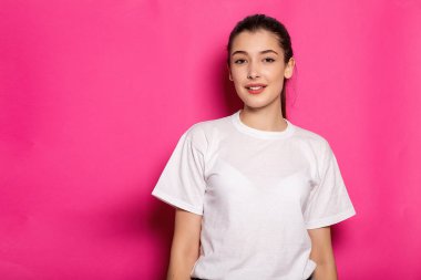 Beyaz tişörtlü çekici kadın pembe arka planda duruyor. Model.