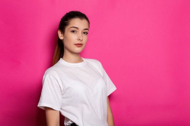 Beyaz tişörtlü güzel bir kadın pembe arka planda duruyor. Model.