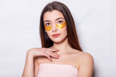 Göz altı maskeli güzel bir kadın. Doğal makyajlı ve yeni cildinde altın renkli kolajen bantları olan güzel bir kadın. Yüksek Çözünürlük