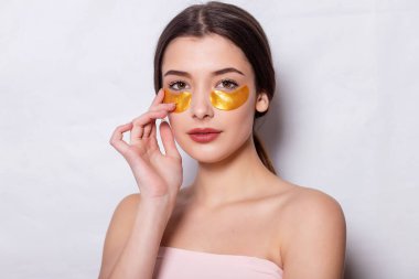 Göz altı maskeli güzel bir kadın. Doğal makyajlı ve yeni cildinde altın renkli kolajen bantları olan güzel bir kadın. Yüksek Çözünürlük
