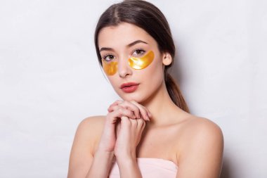 Göz altı maskeli güzel bir kadın. Doğal makyajlı ve yeni cildinde altın renkli kolajen bantları olan güzel bir kadın. Yüksek Çözünürlük