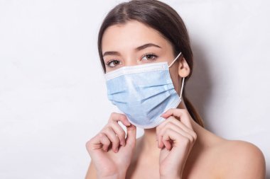 Hava, beyaz arka plan ve fotokopi alanı yüzünden tıbbi maske takan güzel bir kadın. Kadın tıbbi bir maskenin arkasına saklanıyor, beyaz arka plan, kopyalama alanı