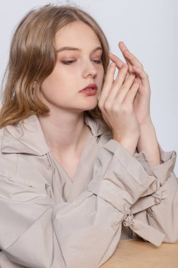 Bir bardak suyla gülümseyen genç kadın, stüdyoda poz veren bej yağmurluklu güzel kız.