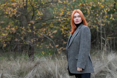 Ormanda yürüyen güzel kızıl saçlı aktif bir kız. Baharda güzel bir kız, harika bir model, genç seksi bir yetişkin, ormandaki kız, kameraya bakıyor, açık havada, uzun saçlı, sıradan bir öğrenci kız.