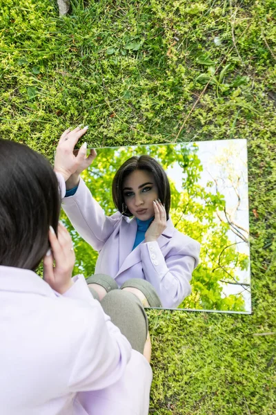 illusion portrait Stylish girl in sun glasses and dress sit on sea beach holding mirrors with reflection of sand and stones. New vision of fashion projects concept. Digital narcissism