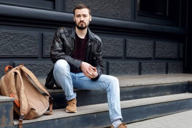 Tasarımcıdan sırt çantalı erkek turistin tam boy portresi karşıdan karşıya geçiyor ve kameraya bakıyor.