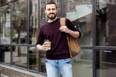 Şapkalı, gülümseyen, modaya uygun bir adam, şehirde elinde bir fincan kahveyle yürüyor. Gülümseyen 30 'lu yaşlardaki gözlüklü bir adamın şehir caddesinde yürüdüğünü ve elinde kahve olduğunu hayal et.