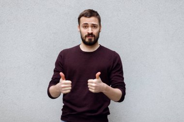 Neşeli, gülümseyen bir adam işaret veriyor. Gri bir arka planda. Tişörtlü ve beyaz tişörtlü bir adam sınıfı parmaklarıyla gösteriyor.