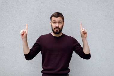 Mavi giyinmiş gülümseyen genç adam, bir yere geliyor ya da mesaj ya da slogan için yer kopyalıyor, gri arkaplan üzerinde el işareti hareketi yapıyor. Duygular ve başarı kavramı.