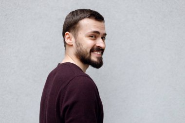 Beyaz tişörtlü, gri arkaplanda izole bir şekilde kameraya bakan gülümseyen yakışıklı adamın portresini yakından çek.