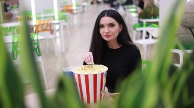 Genç kız patlamış mısır yemeden önce kafede oturuyor. Genç bir kadın kameraya patlamış mısır atıyor. Hamile kadın eğleniyor ve mutlu..