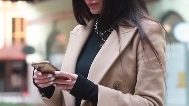 在现代化的大楼附近 一个微笑的女商人正在用智能手机发短信 城市街道背景下的年轻女性在手机上使用应用程序 — 图库视频影像