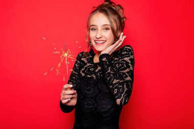 Havai fişekler ve insan konsepti - gülümseyen genç kadın ya da genç kız maytaplı mutlu kadın kırmızı arka planda siyah elbiseyle kutluyor. Kız şaşırdı.