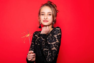 Havai fişekler ve insan konsepti - gülümseyen genç kadın ya da genç kız maytaplı mutlu kadın kırmızı arka planda siyah elbiseyle kutlama yapıyor.