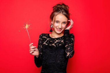 Havai fişekler ve insan konsepti - gülümseyen genç kadın ya da genç kız maytaplı mutlu kadın kırmızı arka planda siyah elbiseyle kutluyor. Kız kameraya gülümsüyor.