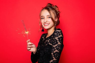 Havai fişekler ve insan konsepti - gülümseyen genç kadın ya da genç kız maytaplı mutlu kadın kırmızı arka planda siyah elbiseyle kutluyor. Kız kameraya gülümsüyor.